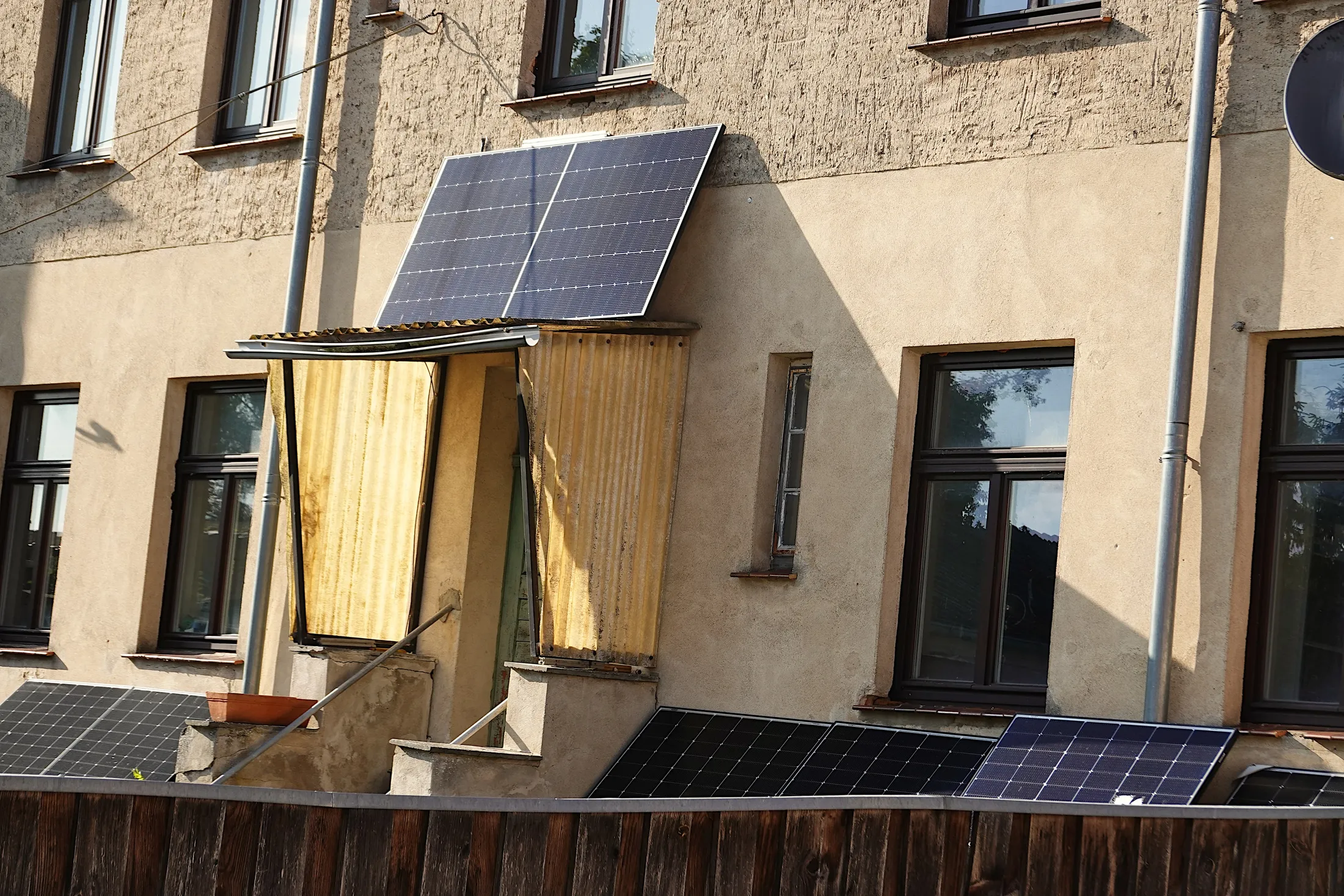 Altbaufassade mit zwei Solarmodulen über einem Vordach und weiteren Modulen entlang der Balkonbrüstung darunter.