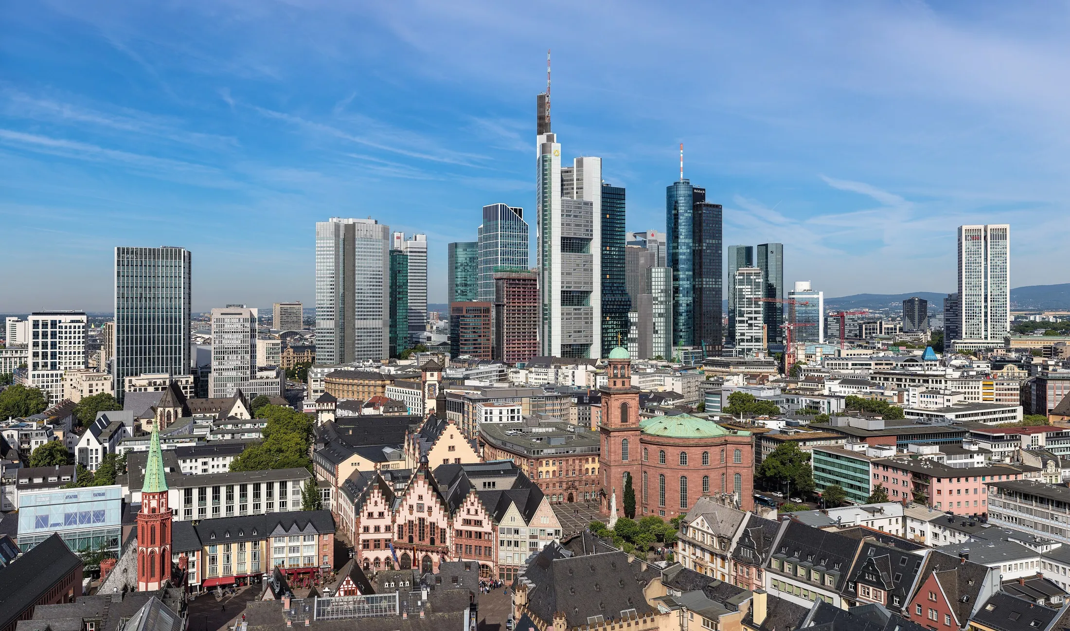 Blick über die Dächer der Frankfurter Altstadt mit Römer, Paulskirche und Nikolaikirche, dahinter die Hochhäuser des Bankenviertels unter blauem Himmel.